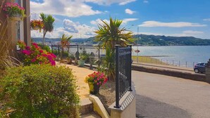 A coastal street with a sidewalk, a metal fence, and a car parked by the road. - Corriemar Guest House (Oban)