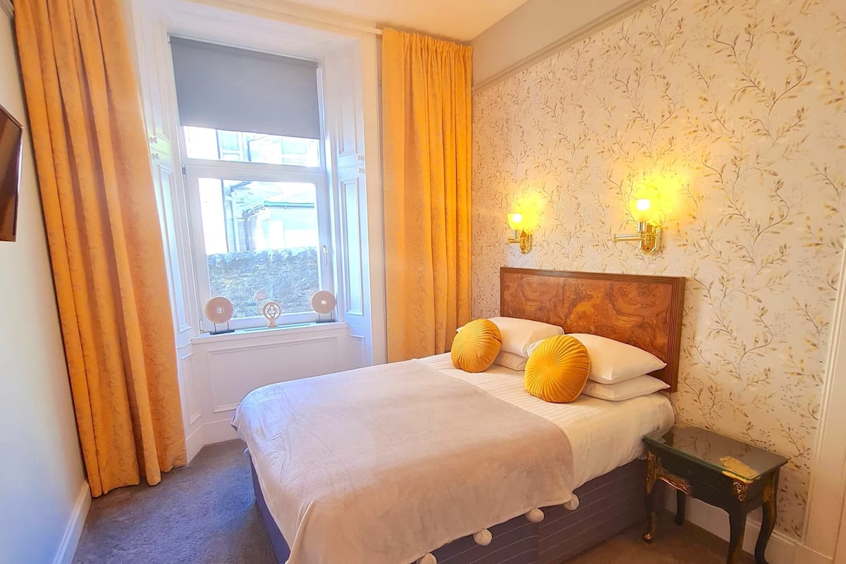 A bedroom with a bed, curtains, a window, and wall-mounted lights.