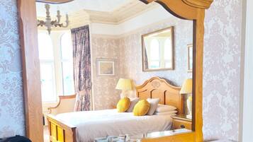 A bedroom with a large mirror, wooden furniture, a bed with yellow pillows, and a bedside table with a kettle and a tray of snacks.