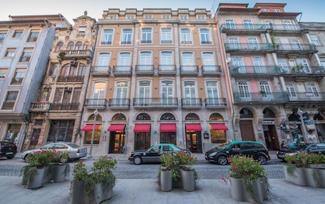 A row of multi-story buildings with balconies, a cobblestone street, and potted plants.