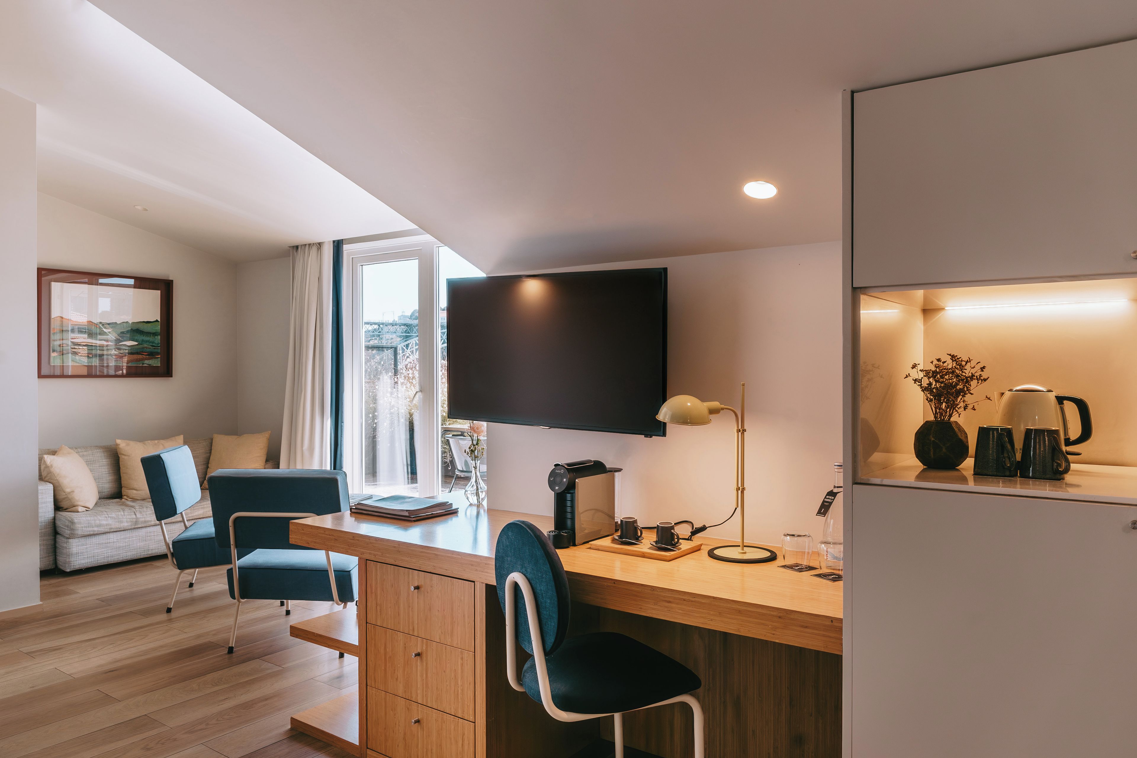 Une chambre moderne équipée d’un bureau, de chaises, d’un téléviseur à écran plat, d’une machine à café et offrant une vue sur l’extérieur.