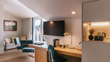 Une chambre moderne équipée d’un bureau, de chaises, d’un téléviseur à écran plat, d’une machine à café et offrant une vue sur l’extérieur.