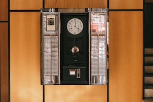 A wall-mounted elevator with a clock, emergency buttons, and a framed certificate.