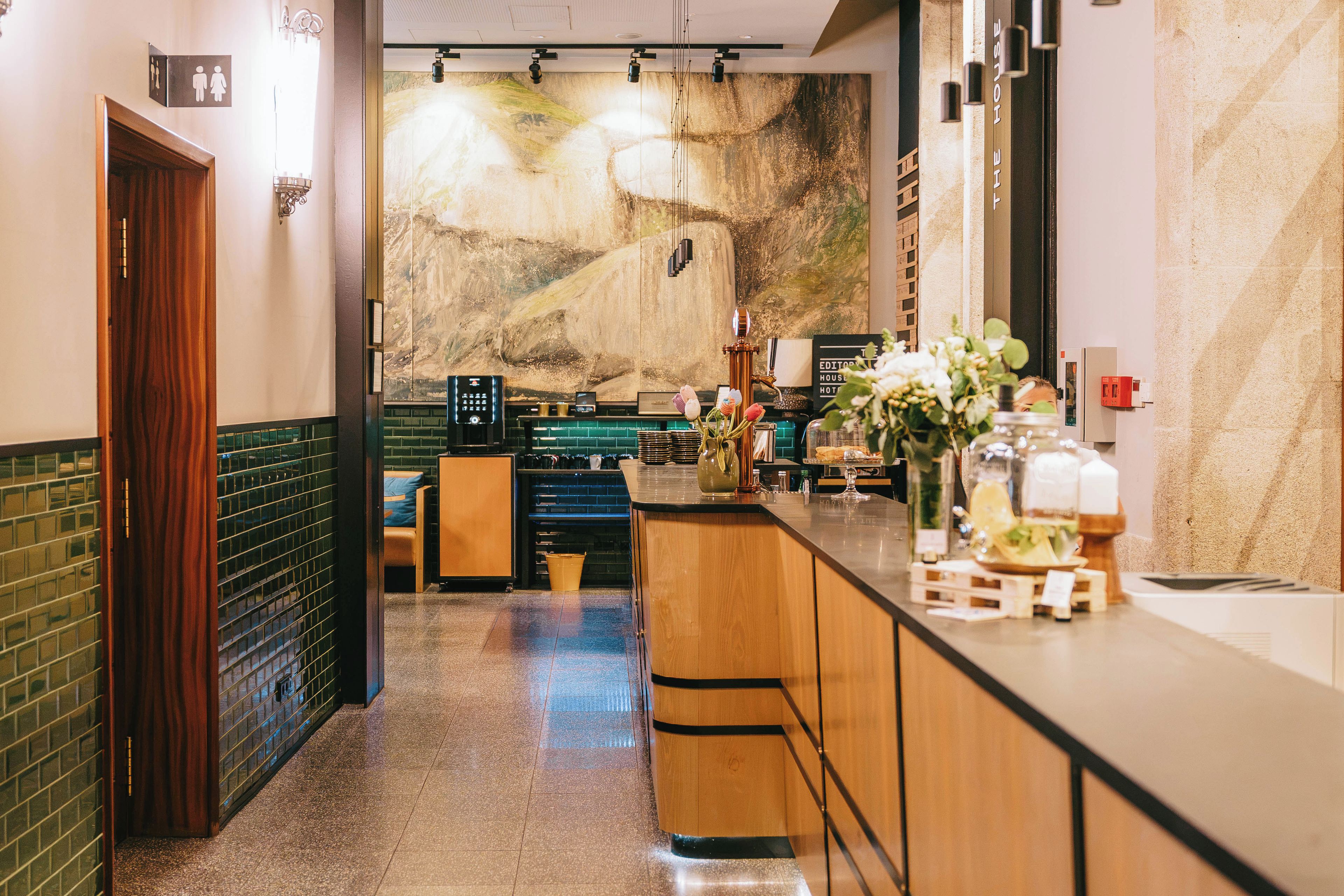Un vestíbul d'hotel amb una zona de bar, una recepció i un mural gran a la paret.