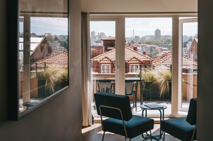 Una habitación con ventanas amplias que ofrecen vistas a edificios de tejados rojos y una torre distante.