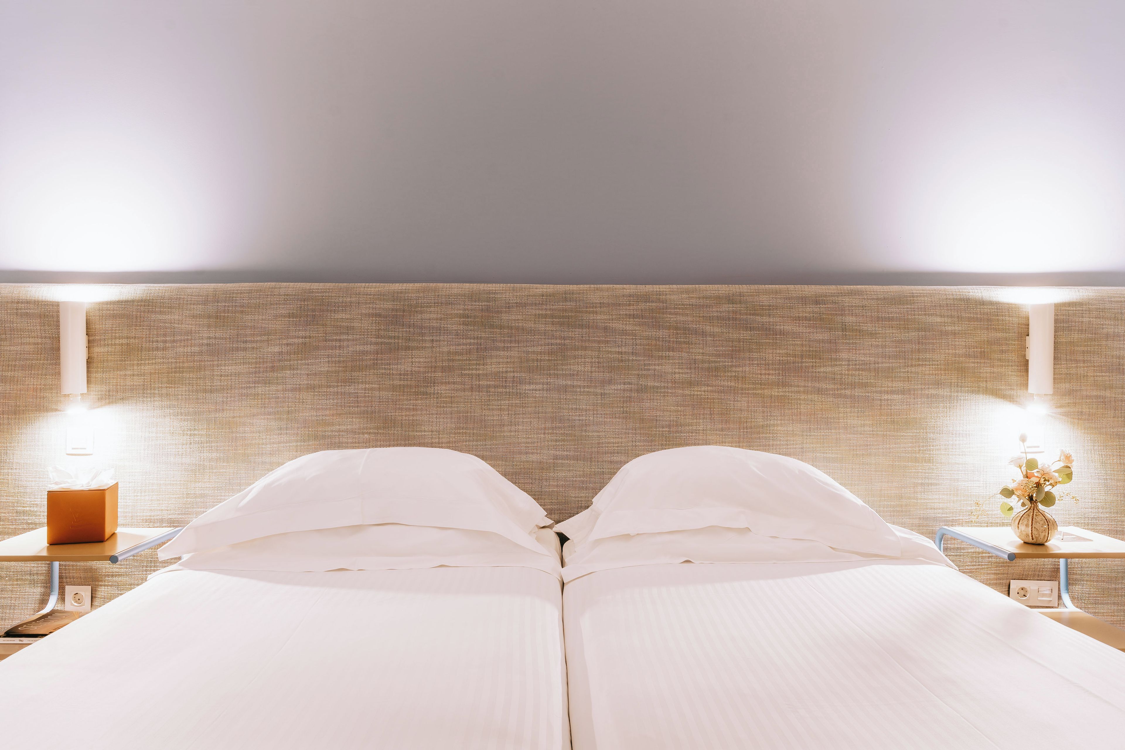 Un lit double avec du linge de lit blanc, deux tables de chevet avec des lampes et un mur à motifs en arrière-plan.