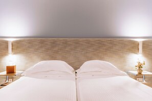 Uma cama de casal com roupa de cama branca, duas mesas de cabeceira com abajures, e uma parede com textura.