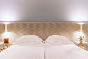 Una cama doble con sábanas blancas, dos mesitas de noche con lámparas y una pared con textura.