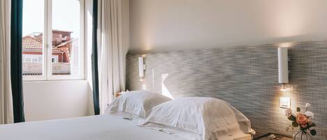 A hotel room with a bed, a nightstand, a vase with flowers, and a window with curtains.