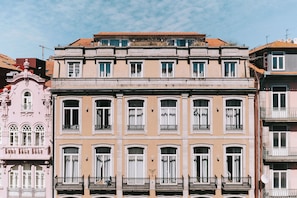 Um edifício de vários andares com fachada simétrica, janelas amplas e varandas com grades de ferro forjado.