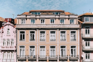 Um edifício de vários andares com fachada simétrica, janelas amplas e varandas com grades de ferro forjado.