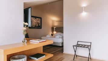 A modern bedroom with a wooden desk, a bed with white bedding, a small table, and a wall-mounted light fixture.