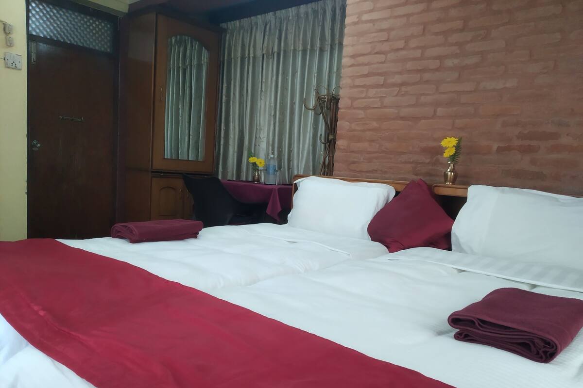 Ein Hotelzimmer mit einem Bett, einem Schreibtisch, einem Sessel, einem Tisch mit Blumen und einer Ziegelwand.