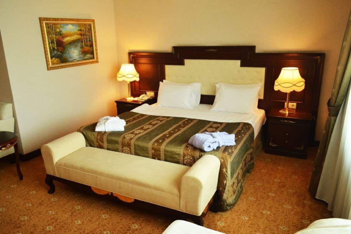 Ein Hotelzimmer mit einem großen Bett, zwei Nachttischen mit Lampen, einer Bank und einem Bild an der Wand.