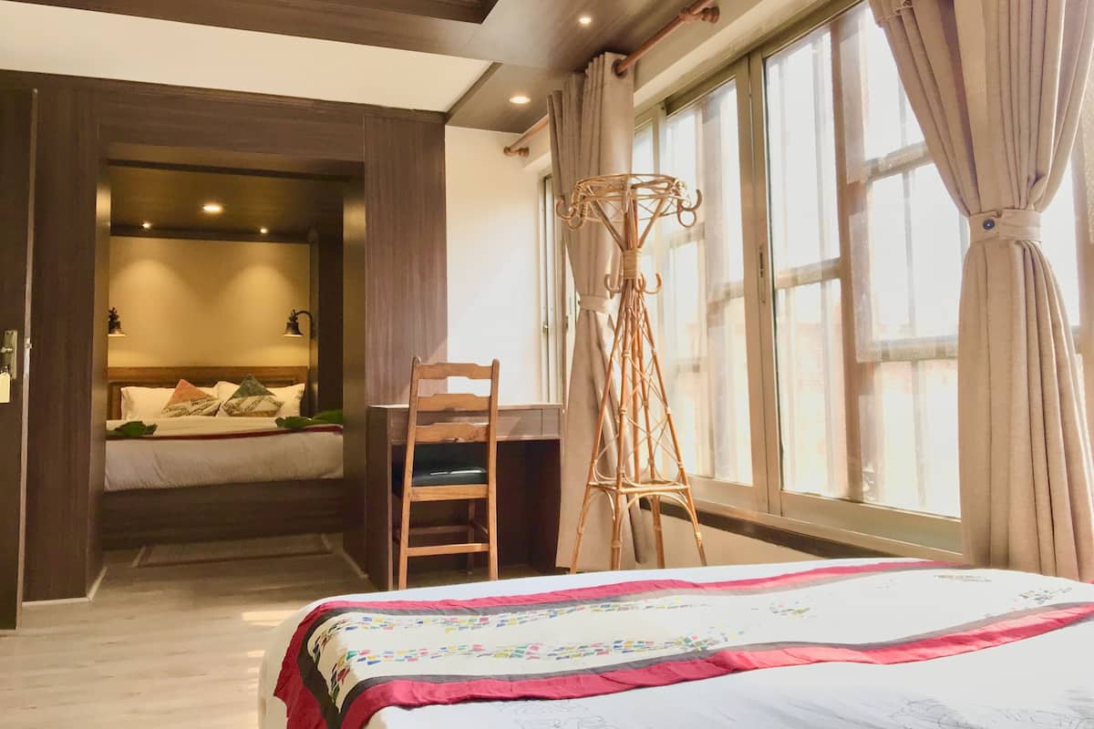 A bedroom with a bed, a desk, and a chair. There is a window with curtains and a view of the outside.