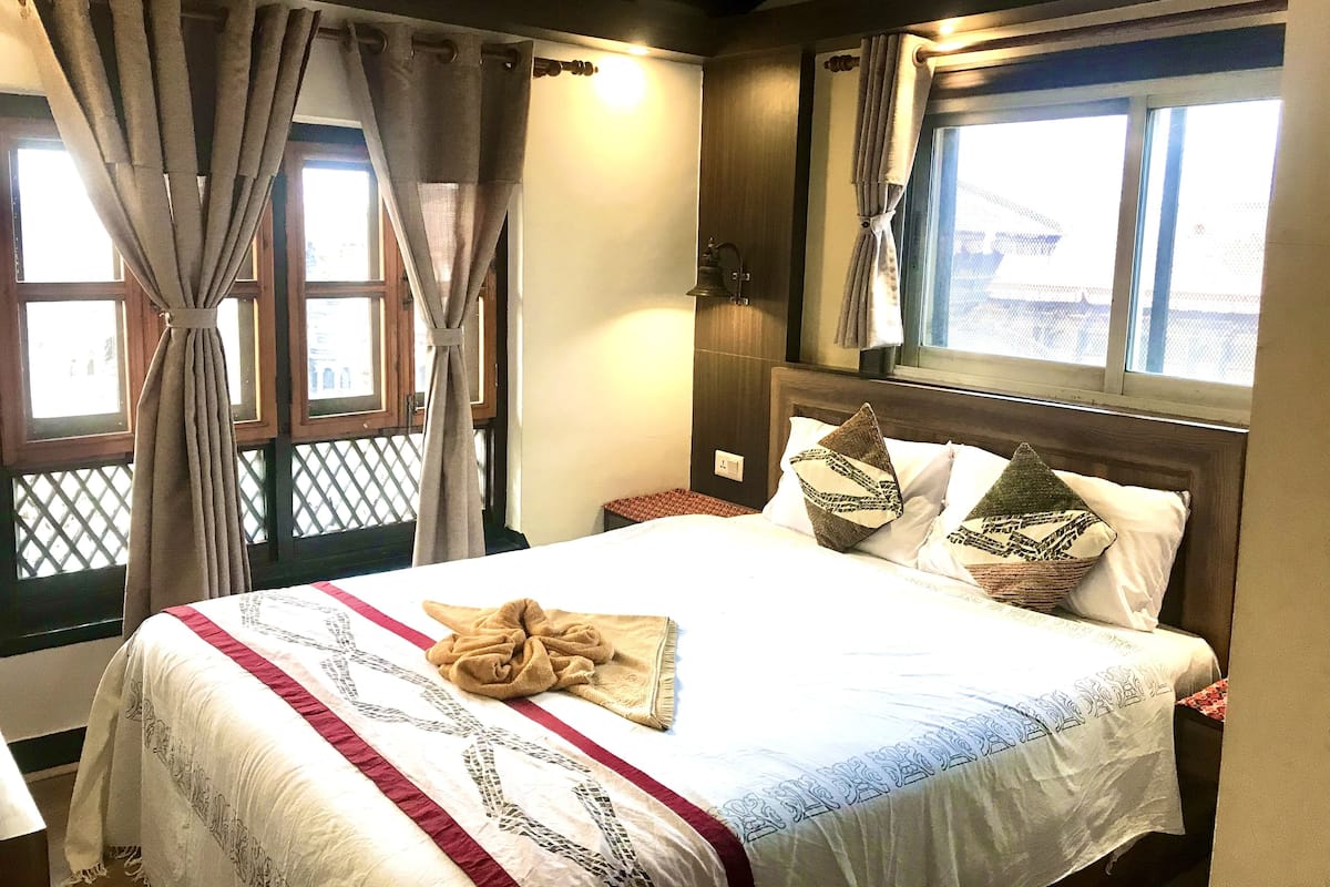 A neatly made bed with patterned bedding, a window with curtains, and a wooden headboard.