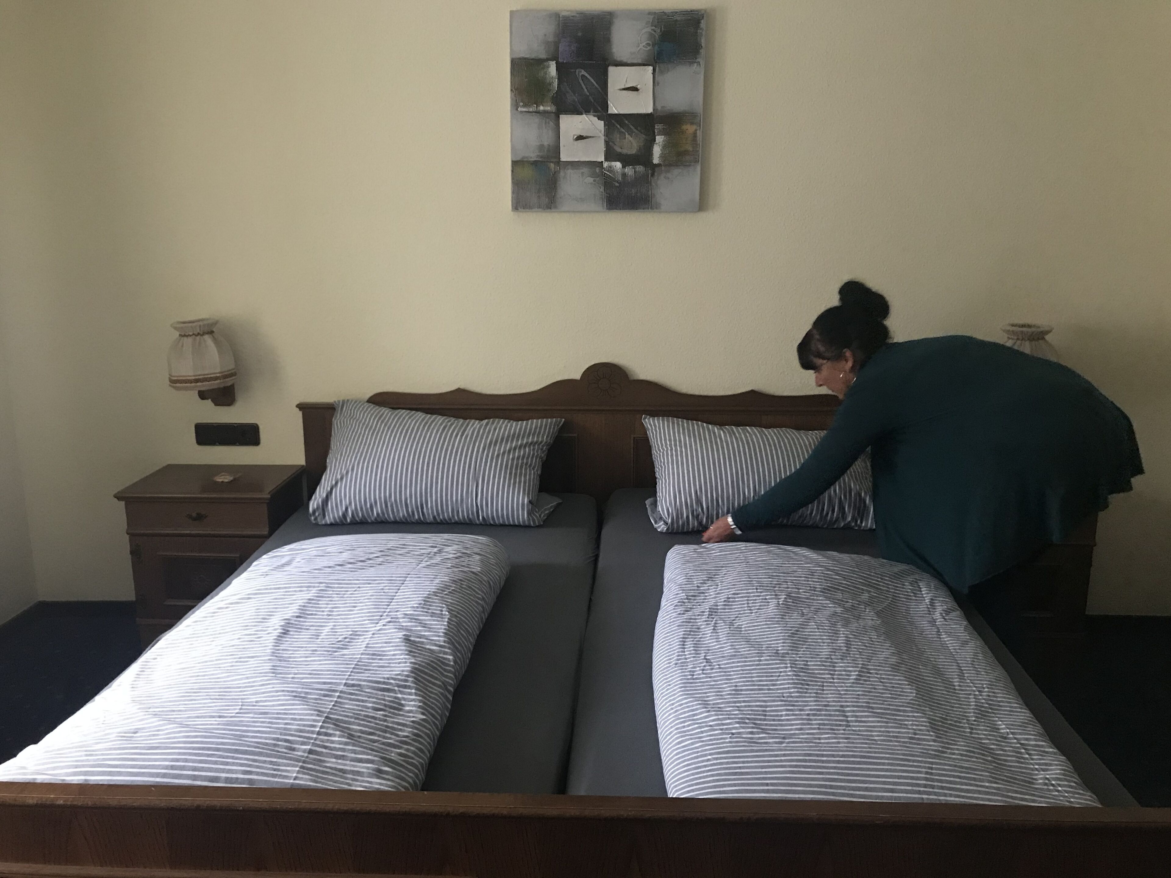 A double bed with striped bedding, a wooden headboard, a nightstand with a lamp, and a wall-mounted artwork.