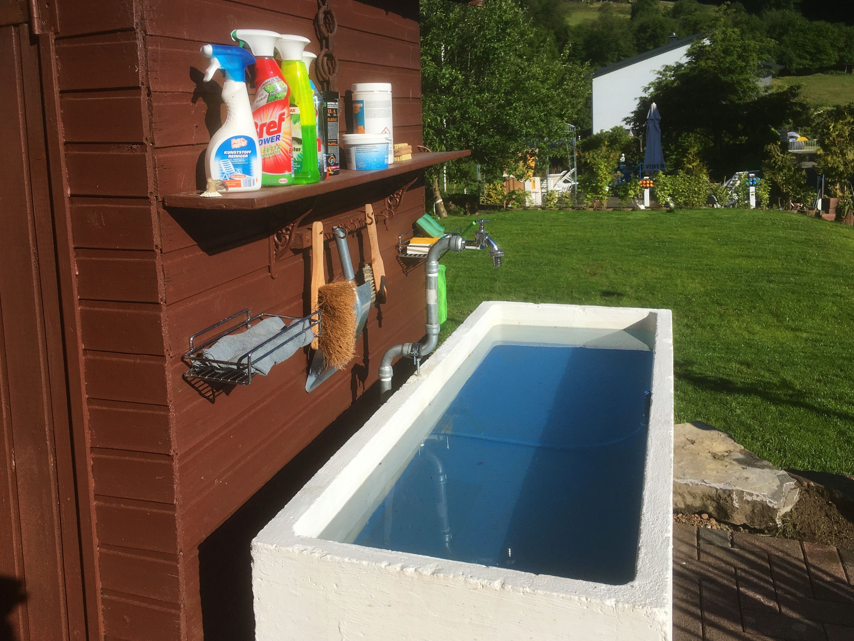 Una piscina con cubierta de madera y un estante con productos de limpieza.