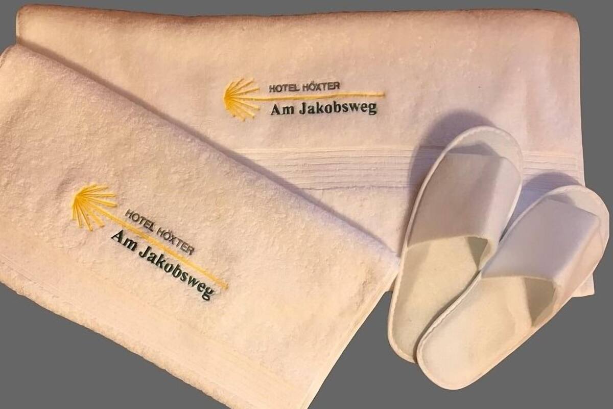 Toalha dobrada e um par de chinelos com bordado mostrando o nome e a localização do hotel.
