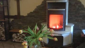 A cozy room with a stone fireplace, a table with a vase of flowers and a glass of red wine, and a stack of firewood.
