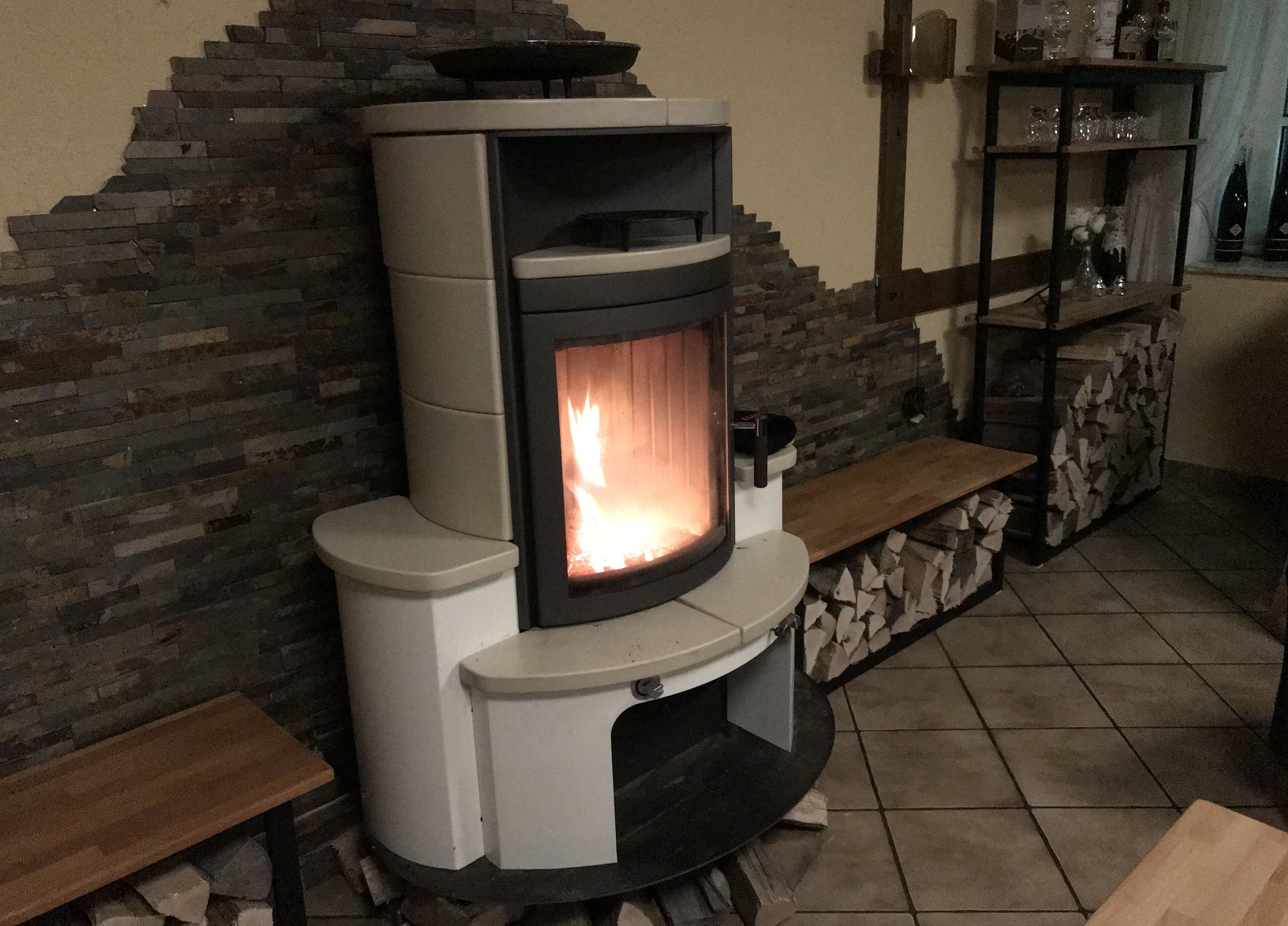 A modern fireplace with a stone wall backdrop, a wooden bench, and a glass display shelf.