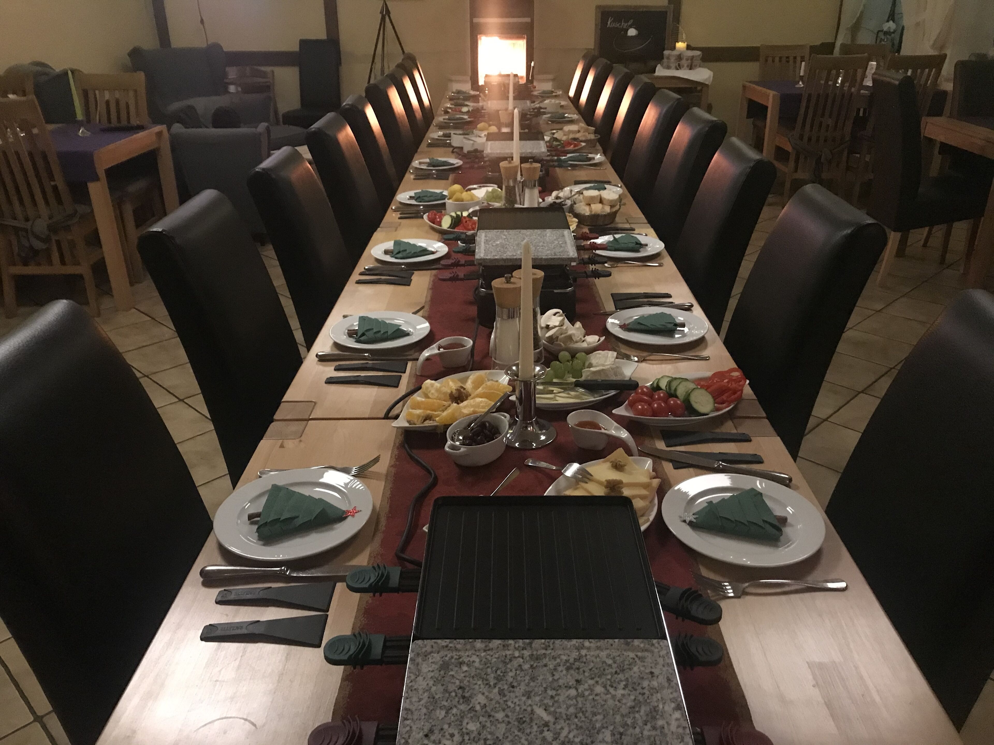 A long dining table set with plates, cutlery, and various food items, surrounded by chairs.