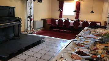 A dining area with a piano, buffet table with various food items, and a stage with lighting equipment.
