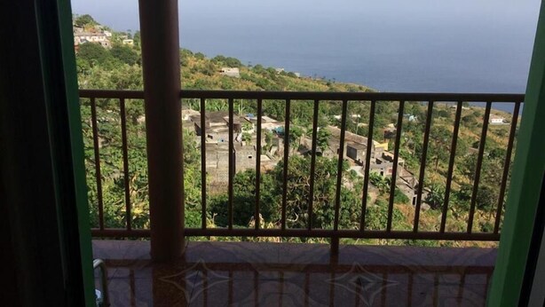 Un balcone con ringhiera metallica affacciato su un paesaggio costiero con edifici e vegetazione.