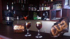Un'area bar con un bancone in legno, due bicchieri di una bevanda scura, una macchina da caffè e scaffali pieni di diverse bottiglie.