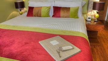 Una cama bien hecha con una colcha roja y verde, dos almohadas y una mesita de noche con una lámpara y un reloj.