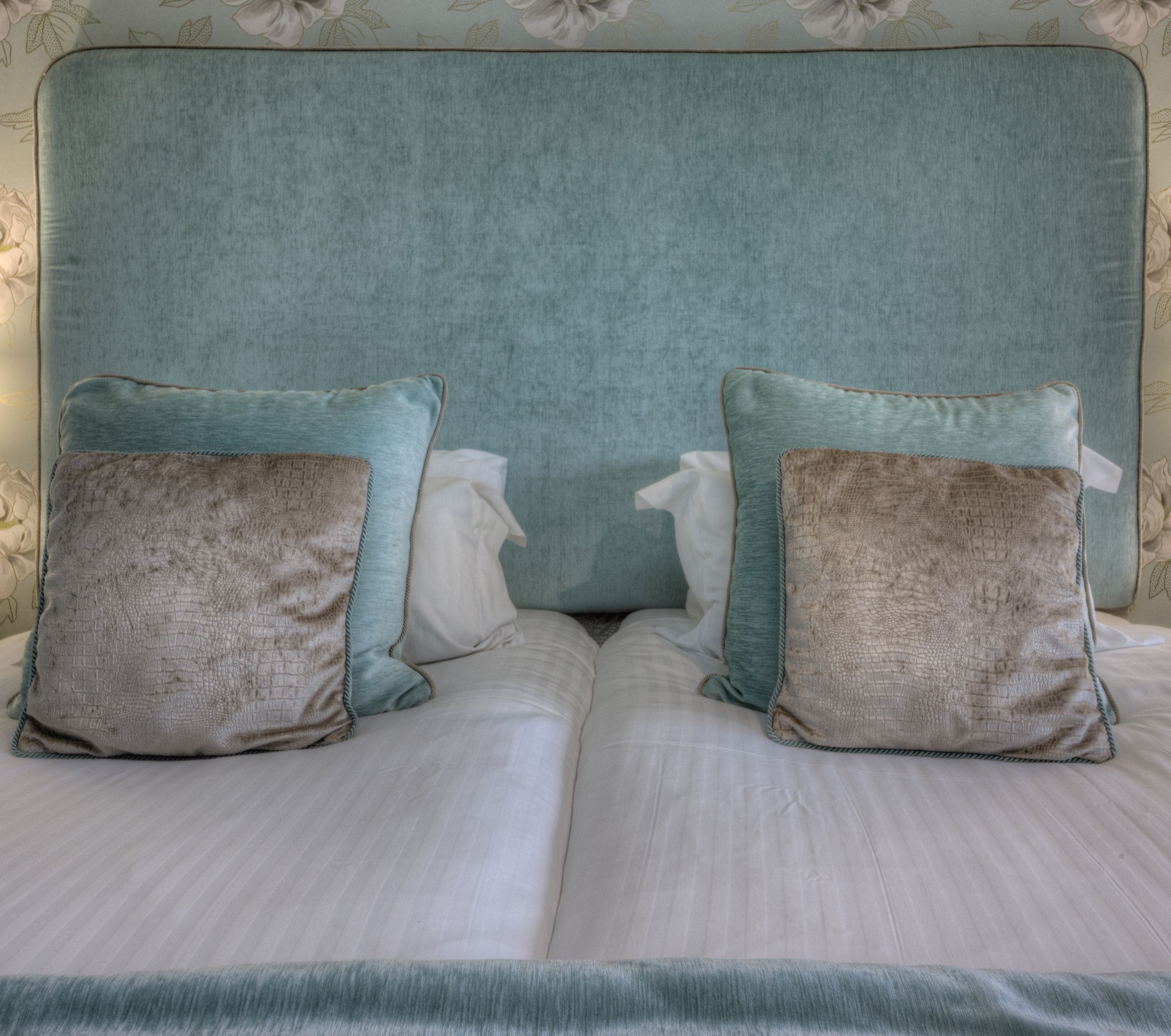 Cama com cabeceira verde-água e dois travesseiros, um verde-água e outro marrom.