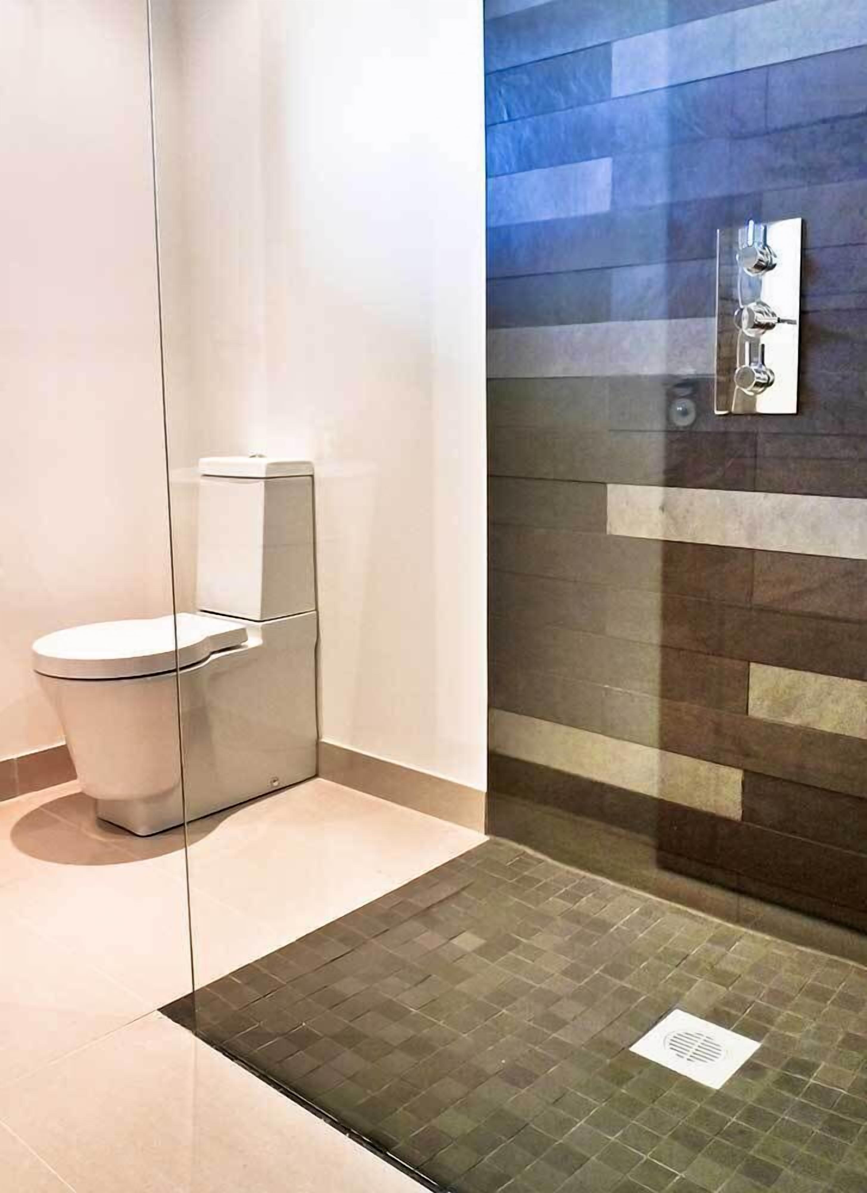A modern bathroom with a glass partition, a white toilet, and a shower area with a tiled wall.
