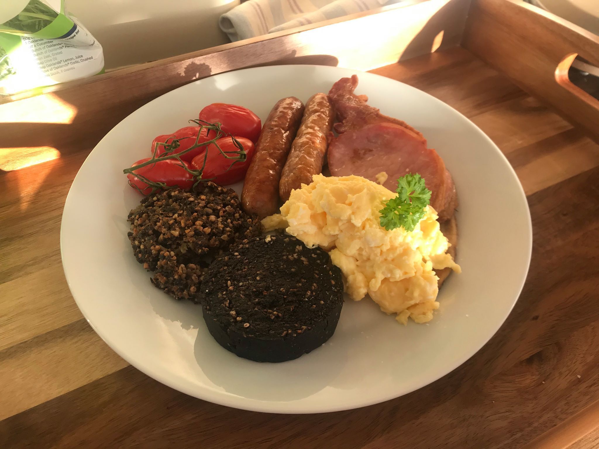 A plate with sausages, tomatoes, scrambled eggs, black pudding, and a slice of ham.