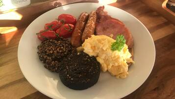 A plate with sausages, tomatoes, scrambled eggs, black pudding, and a slice of ham.
