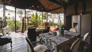 Un comedor con una mesa dispuesta para cuatro personas, rodeada de sillas y un amplio ventanal con vistas a plantas tropicales.