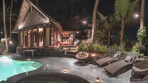 Un resort con piscina, sillas de descanso y una construcción con techo de paja.