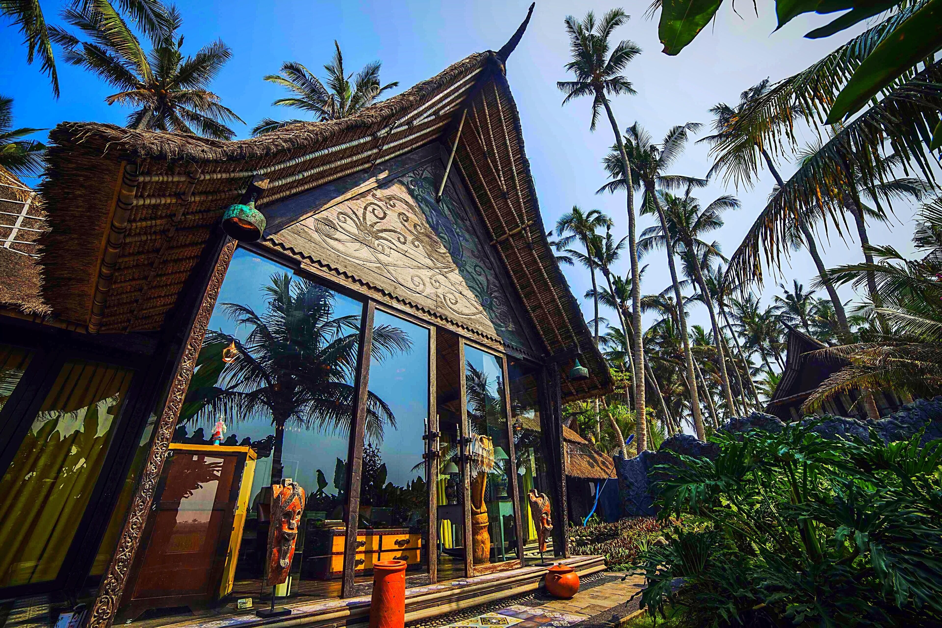A traditional thatched-roof building with large glass windows, surrounded by palm trees.