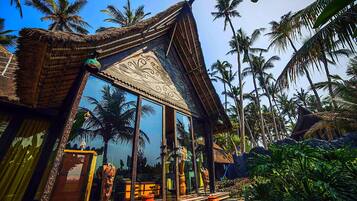 A traditional thatched-roof building with large glass windows, surrounded by palm trees.