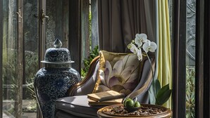 Una habitación con un ventanal grande, una silla, una mesa y un jarrón decorativo.