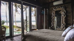 Un dormitorio con una cama grande, un espejo con marco de madera y vistas al océano a través de amplios ventanales correderas.