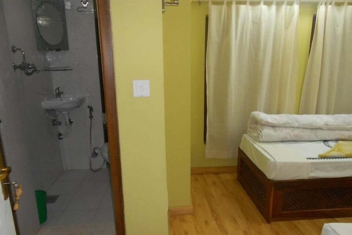 Ein Zimmer mit Holzboden, einem Bett mit weißer Matratze und Kissen, einem grünen Handtuch und einem Badezimmer mit Waschbecken, Spiegel und Dusche.