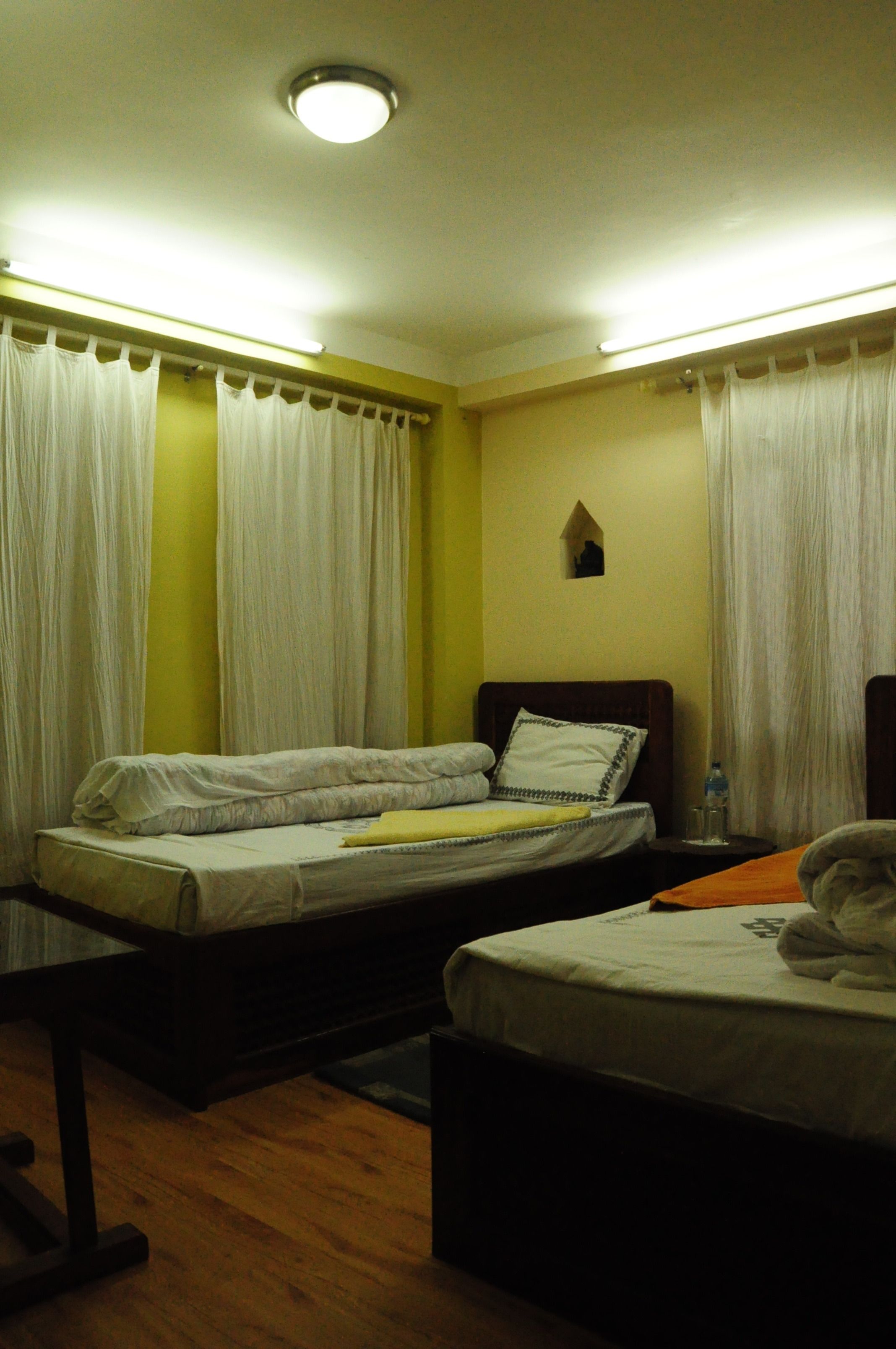A hotel room with two beds, a small table, a nightstand, and a window with curtains.