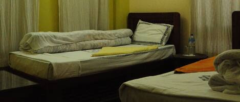 A hotel room with two beds, a small table, a nightstand, and a window with curtains.