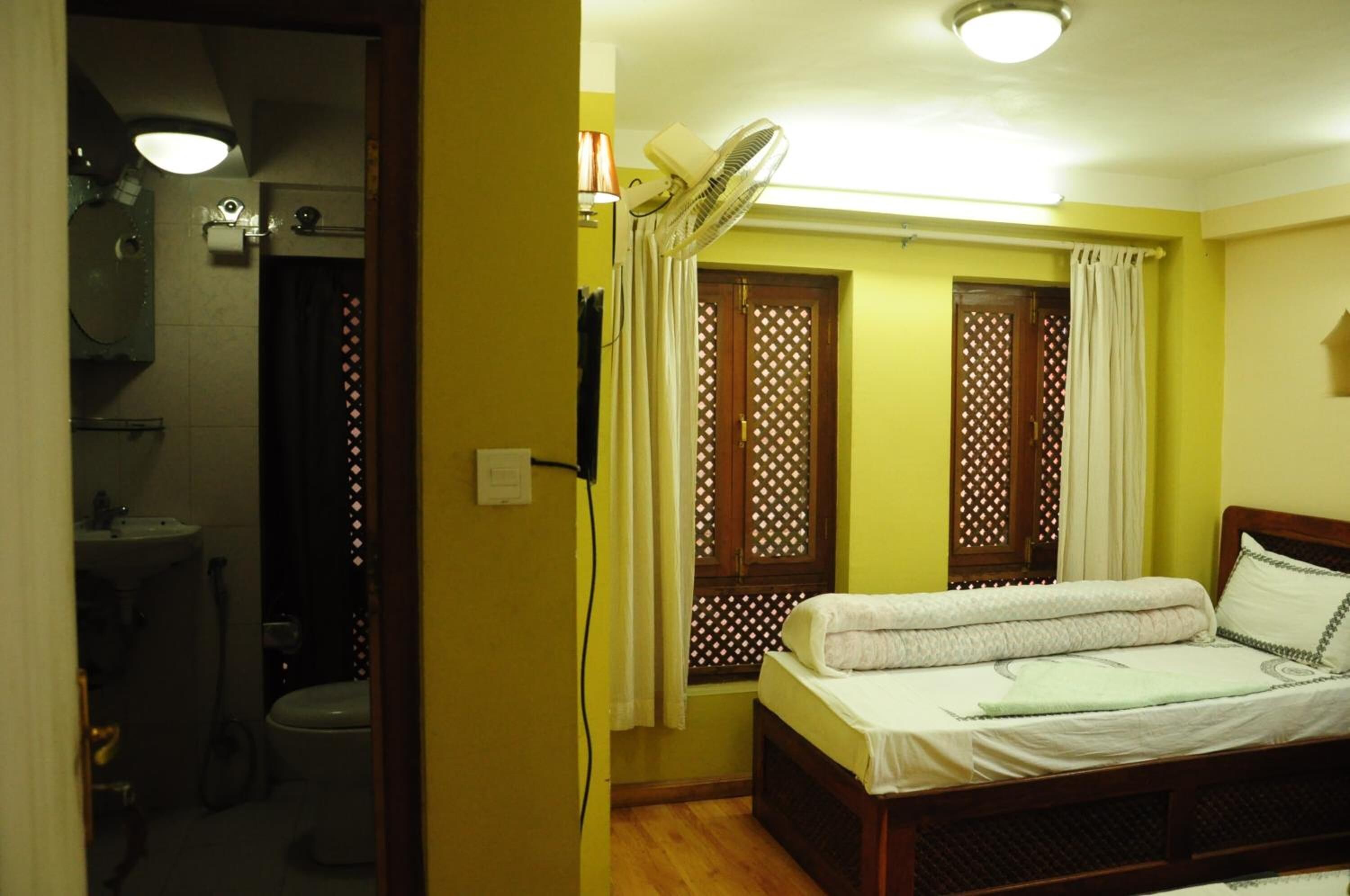 A bedroom with a bed, a bedside fan, and a window with curtains.