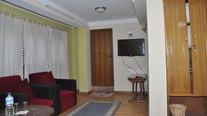 A living room with a sofa, a television mounted on the wall, a wooden door, and a small table with a water bottle. - Sunny Guest House and Cafe (Bhaktapur)