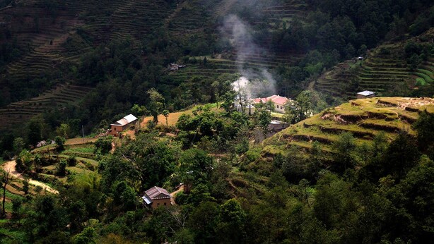 Terraced rice fields, a few houses, and a smoke plume. - Nagarkot Naldum Village Resort (Baluwapati Deupur)