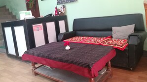 A reception area with a reception desk, a sofa, and a bed with a red blanket. - Mountain Guest House (Bhaktapur)