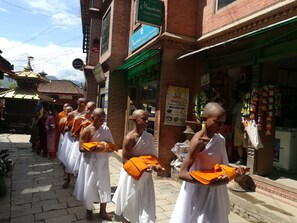 Monks in white robes holding orange scarves, walking past a building with a sign for 'Mountain Guest House'.