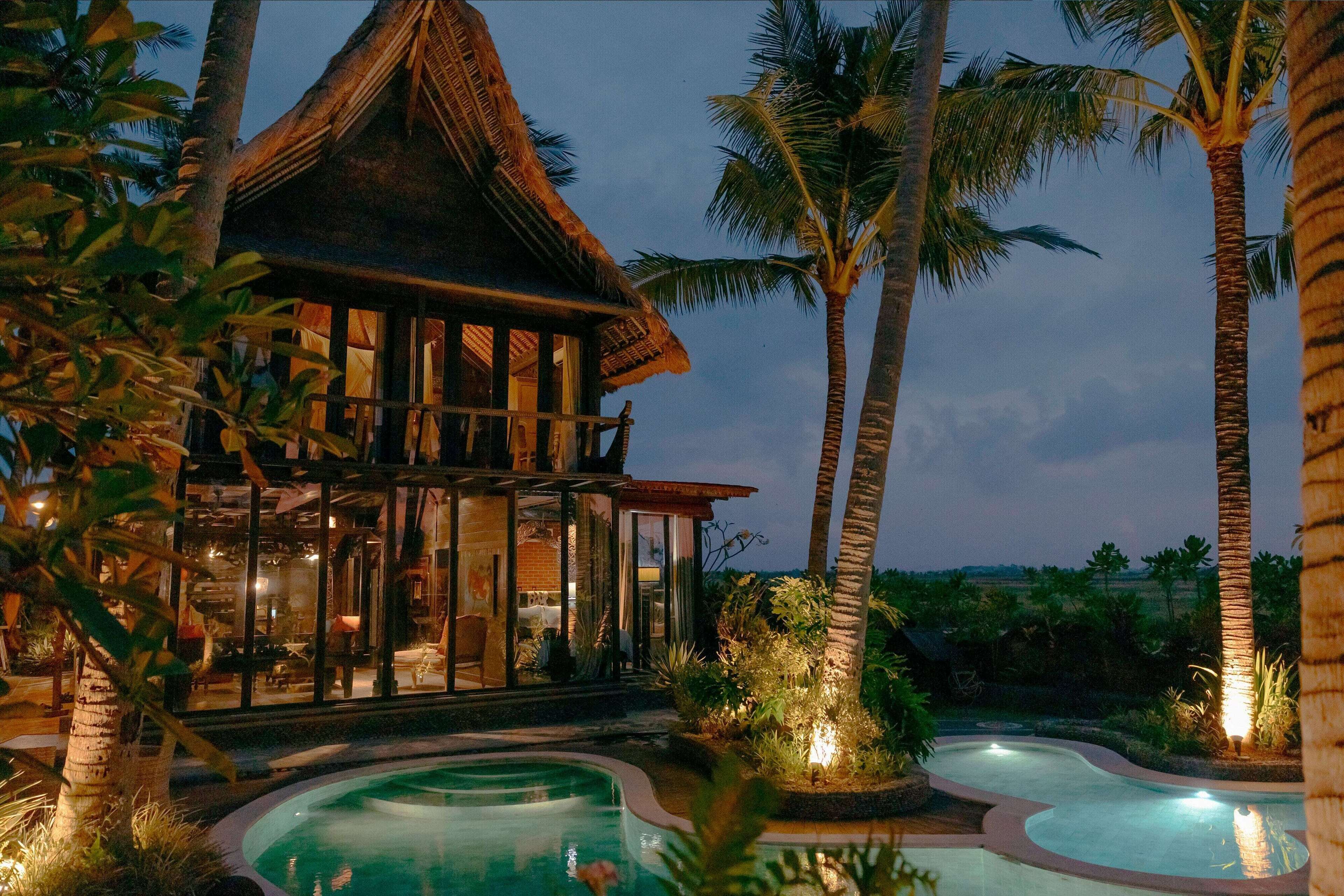 Ein Resort mit Poolbereich, einem Gebäude mit Reetdach und Palmen.