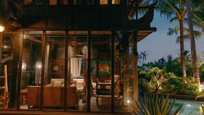 A modern villa with a glass-enclosed living area, a pool, and tropical vegetation. - Most Exotic Beachfront Villa Keong (Tabanan)